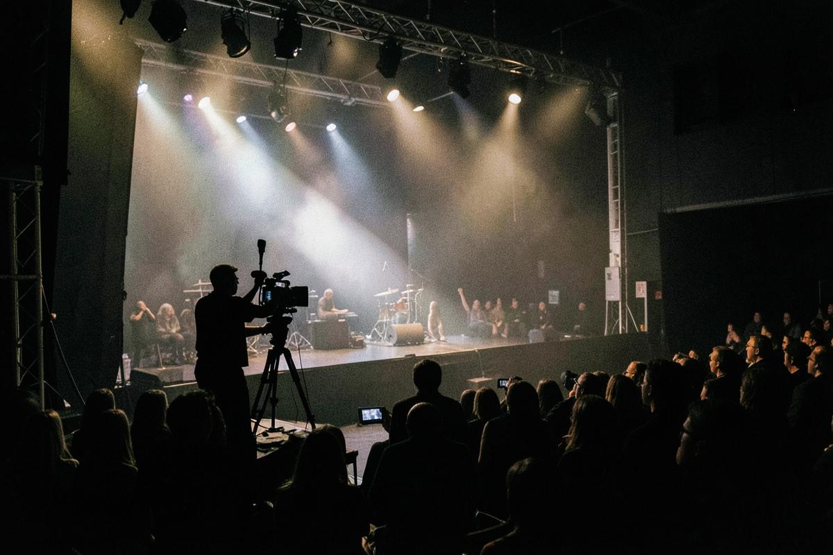 Camera operator silhouetted in the wings during a lit stage performance