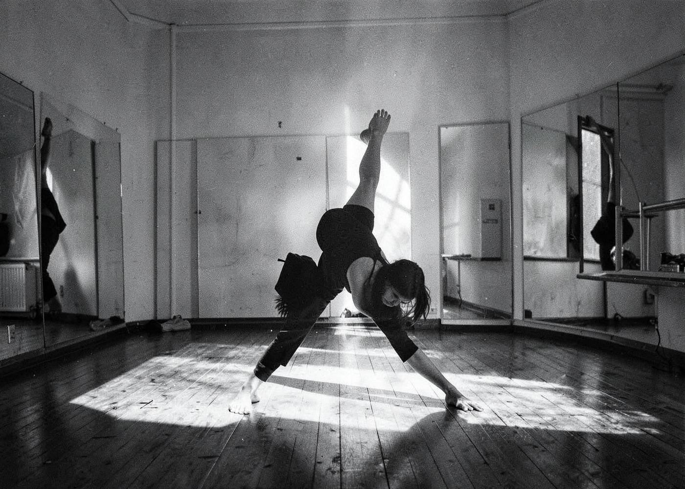 Dancer stretching in a bare rehearsal room lit by daylight through a window