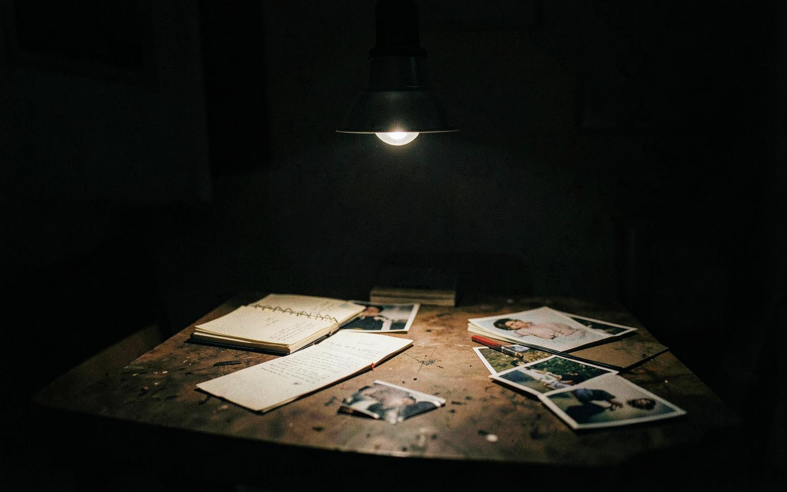 Case notebooks and photographs spread on a table beneath a single hanging lamp