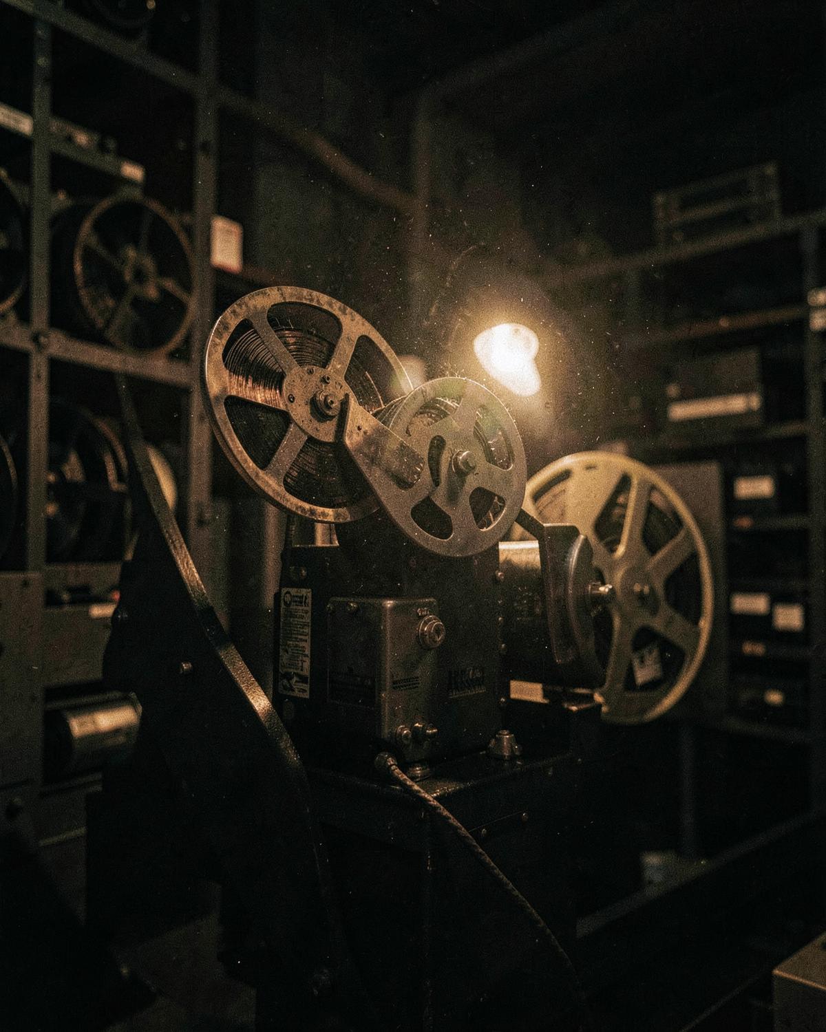 Vintage film projector and reels in a dark archive, lit by a single warm lamp